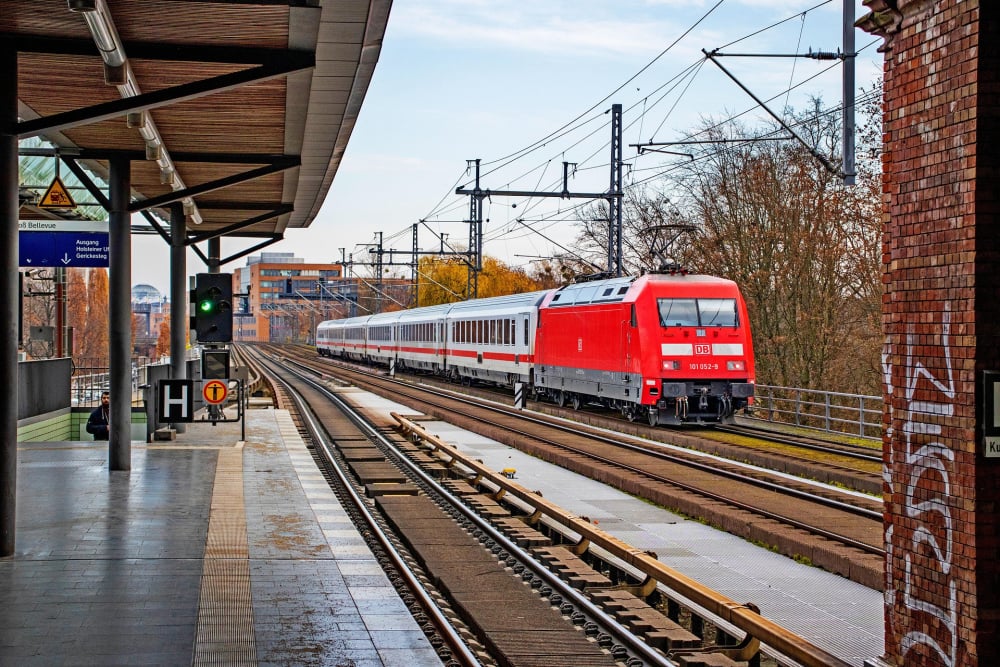 Ansicht eines am Bahnhof durchfahrende Fernzuges mit Lok voraus.