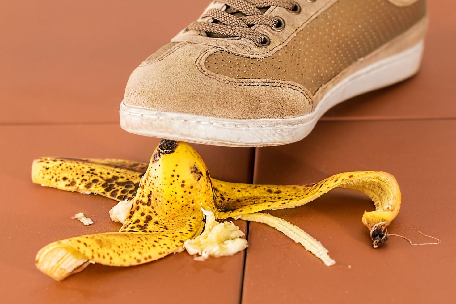 Ein mit einem Turnschuh bekleideter Fußt tritt auf eine Bananenschalte.